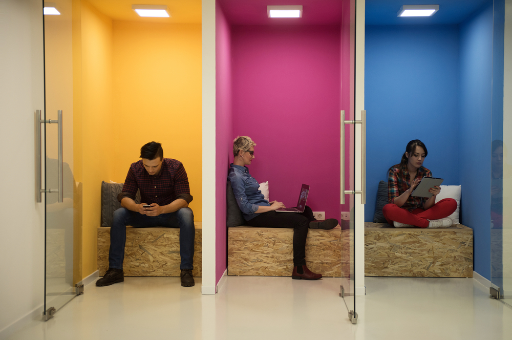 Three individuals working on their devices in separate colorful spaces